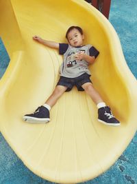 High angle portrait of boy lying on yellow slide at playground