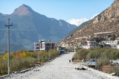 Road by houses and mountains against clear sky