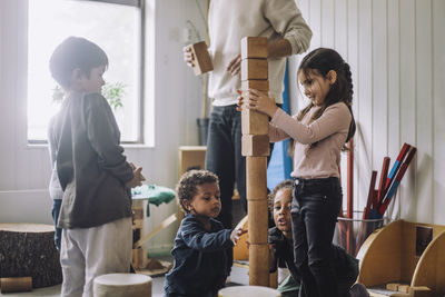 Female and male students stacking wooden toy blocks by male teacher in day care center