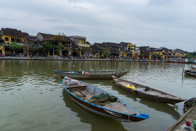 Boats moored on river by buildings against sky