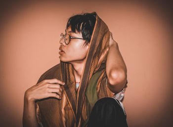 Young man with scarf sitting against wall