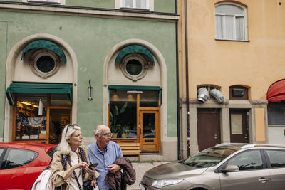 Confused senior man and woman looking away while crossing against building
