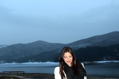 Beautiful young woman standing in lake against mountains
