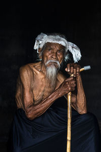 Portrait of man sitting against black background