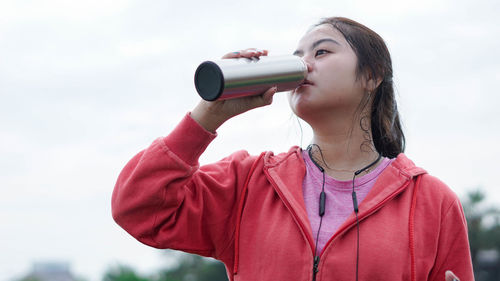 Portrait of beautiful young woman drinking against sky