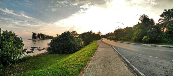 Road by trees against sky during sunset