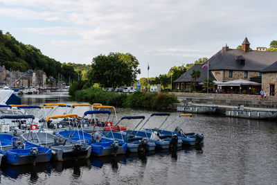 Boats moored in river by buildings against sky