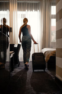 Woman traveler with luggage suitcase after checking into a hotel room looking in the window