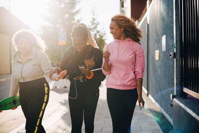 Smiling female friends talking while walking on sidewalk in city