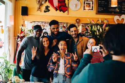 Young man photographing cheerful multi-ethnic friends standing at restaurant during brunch