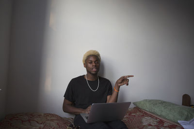 A young man sitting on a bed with a laptop