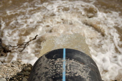 A strong stream of water pouring from a plastic water pipe into a river.