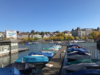 Sailboats moored on river by buildings against clear blue sky