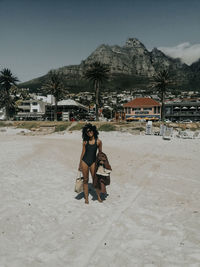 A black woman in a black one-piece swimsuit on camps bay beach, south africa.