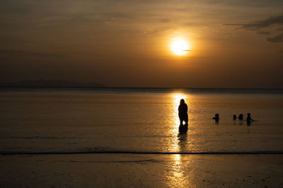 Silhouette people on beach against sky during sunset