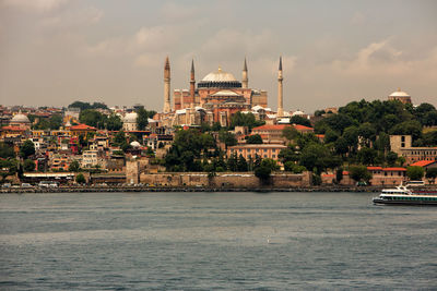 Strait by buildings and mosques against cloudy sky