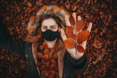 Portrait of young woman standing by maple leaves during autumn