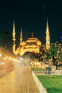 Water fountain by footpath against illuminated sultan ahmed mosque at night