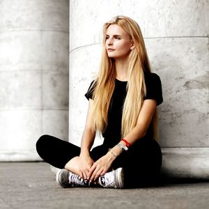 Beautiful young woman sitting against wall