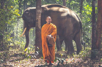 Monk standing by elephant at forest