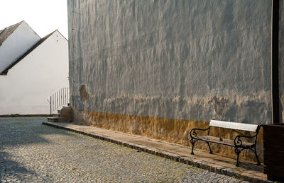 Empty bench on sidewalk against wall