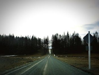 Gravel road with trees against sky