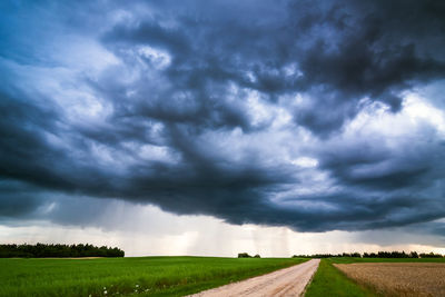 Road passing through field against storm clouds
