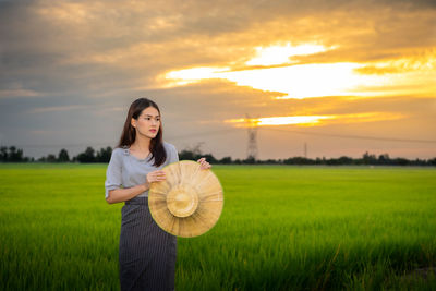 Woman standing on field against sky during sunset