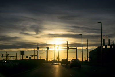 Traffic on road in city against sky during sunset