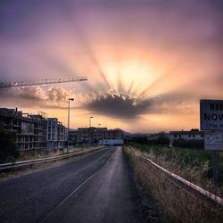 Road by city against sky during sunset