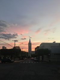 Road by buildings against sky during sunset