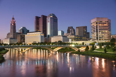 Bridge over river by buildings against sky in city