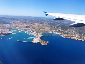 Aerial view of airplane wing over sea against clear blue sky