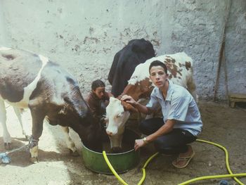 Portrait of man with sister feeding cows against wall