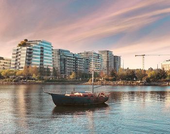 Boats in river by buildings against sky at sunset