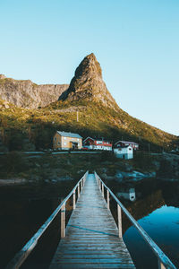 Pier amidst mountains against clear blue sky