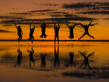 Silhouette people on beach against sky during sunset