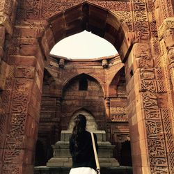 Rear view of woman standing by historic archway at qutb complex