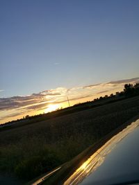 Road by silhouette field against sky during sunset