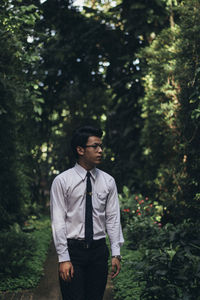 Young man standing on footpath amidst trees in park