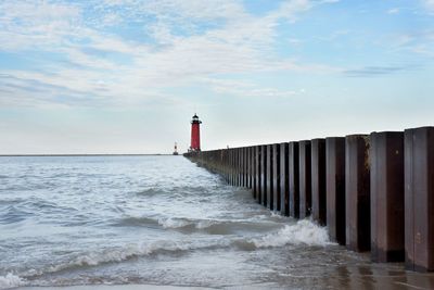 Lighthouse on sea by building against sky