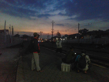 People standing on road against sky at sunset