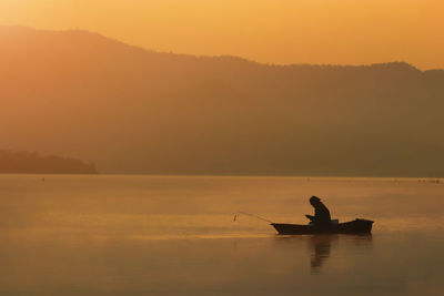 Silhouette fishing man sitting and look smart phone in his boat with sunset flare effect