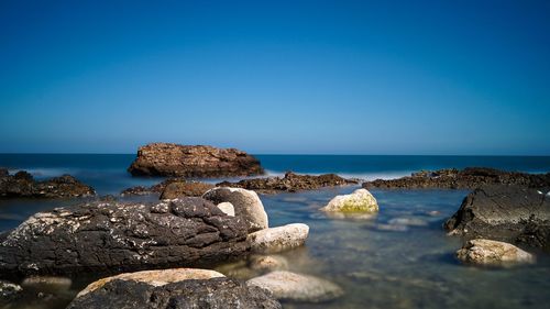 Rocks on beach against clear blue sky