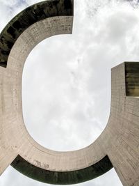 Low angle view of concrete public sculpture  against cloudy sky