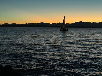 Silhouette sailboat sailing on sea against clear sky during sunset