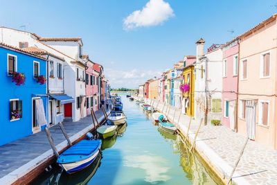 Boats moored on wooden post amidst buildings against sky