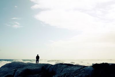 Rear view of man on beach stones against sky