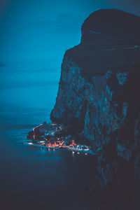 Illuminated rock formation in sea against blue sky at night