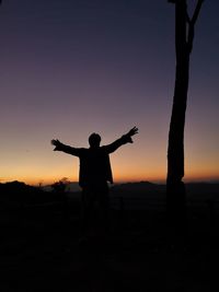 Silhouette man with arms outstretched standing on field against clear sky during sunset